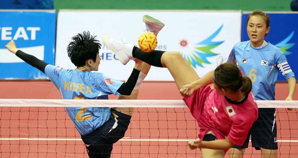 Two sepak takraw players kicking high.
